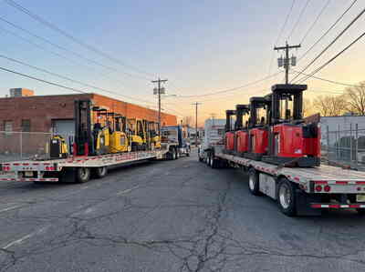 Flatbed trailers loaded with forklifts outside a BidWorx warehouse